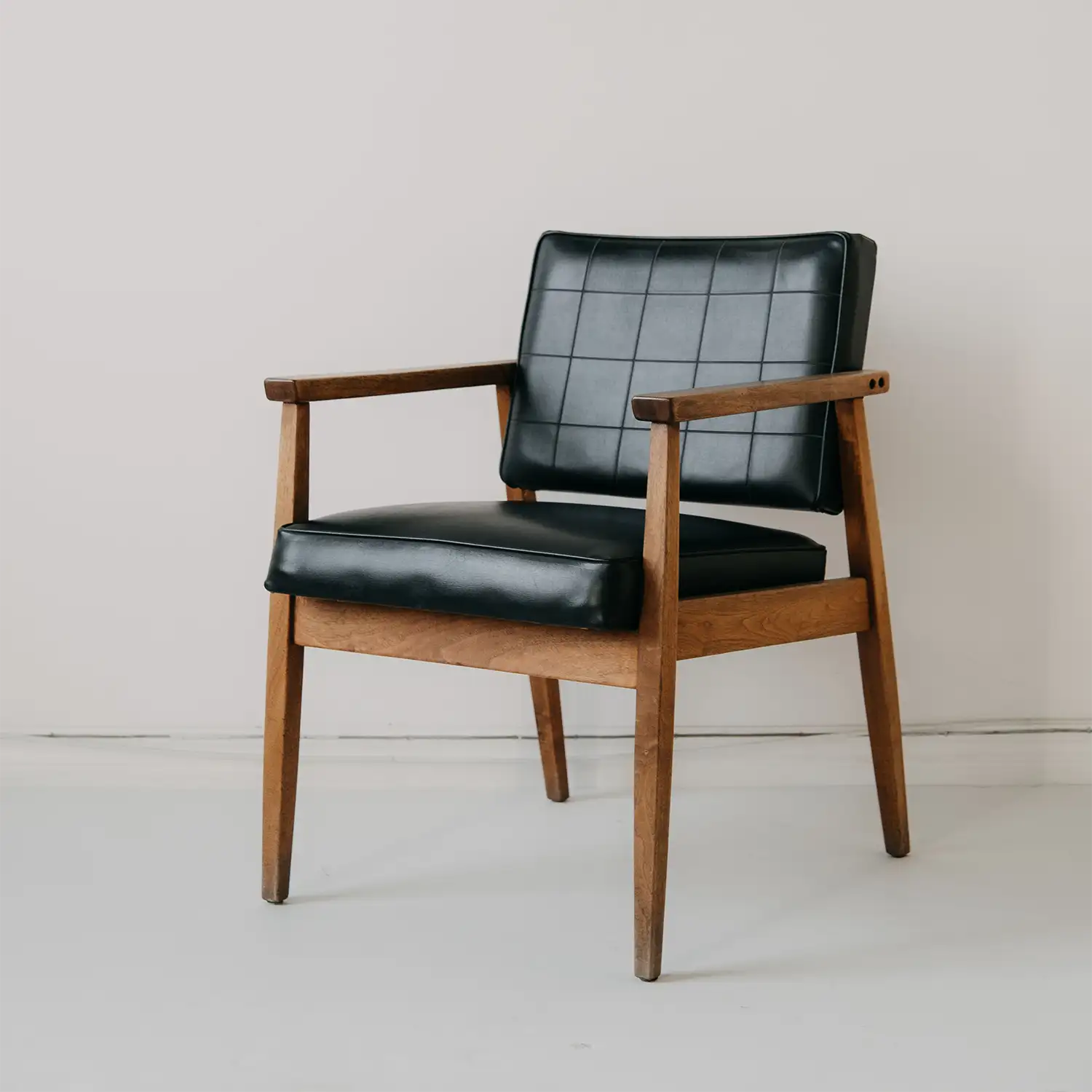 Wooden armchair with black padded seat and backrest against a light wall